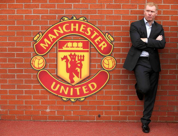 Former Manchester United player Scholes stands next to a team emblem before their English Premier League soccer match against Everton at Old Trafford in Manchester