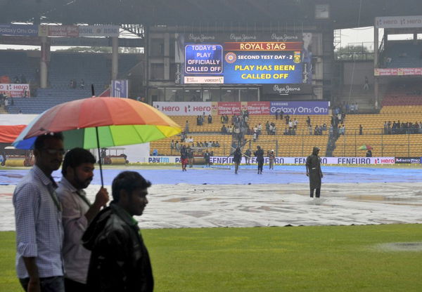 Groundsmen walk under an umbrella after steady drizzle washed out entire second day&#8217;s play in second test cricket match between India and South Africa in Bengaluru