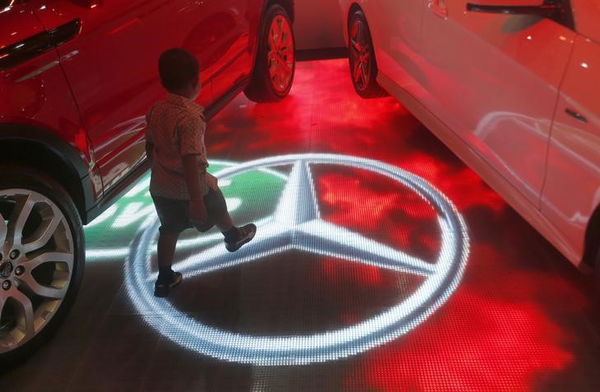 A boy walks past a Mercedes Benz logo on an electronic board at Colombo motor show