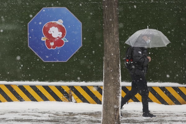 A man walks in the snow near a picture of the Beijing 2022 Winter Paralympics mascot Shuey Rhon Rhon in Beijing