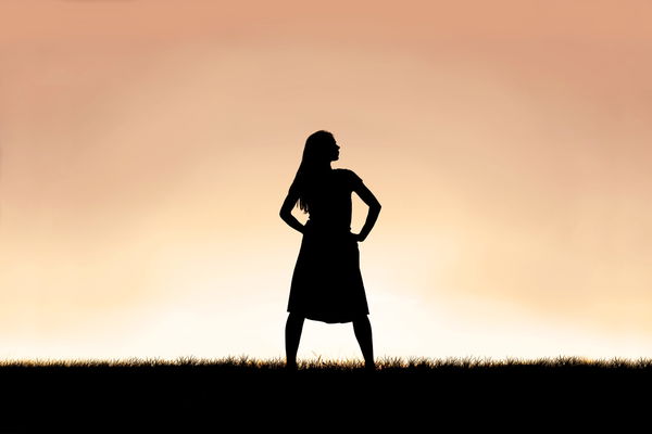 The  silhouette  of  a  strong,  beautiful  woman  stands  isolated  against  a  sunset  in  the  sk