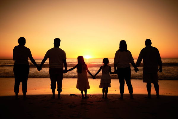 Big family silhouette on beach with sea waves, sunset on the horizon and holding hands for development wellness, support